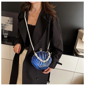 Detailed close-up of blue acrylic shell bag featuring white pearl straps and gold clasp