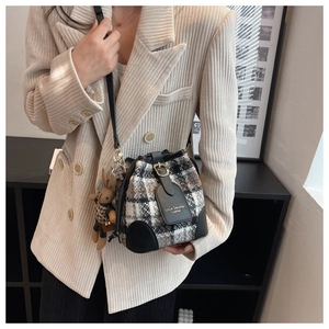 Détail du sac seau en tweed à carreaux avec garniture en cuir noir et breloque ours