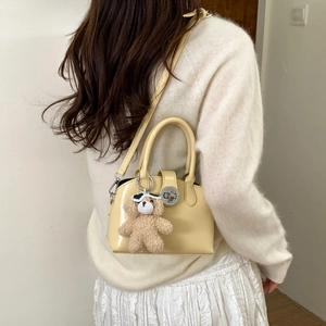 Detail of creamy yellow glossy handbag with silver lock and plush bear charm on white knit