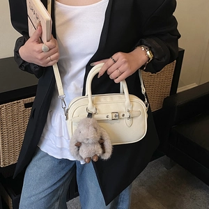 Close-up of cream textured crossbody bag with leather strap buckle and plush bunny charm