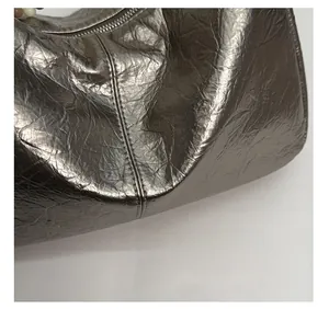 Détail du sac à bandoulière argenté montrant la texture plissée et les coutures