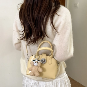 Close-up of cream-colored shell bag featuring a metal lock and a cute plush bear charm