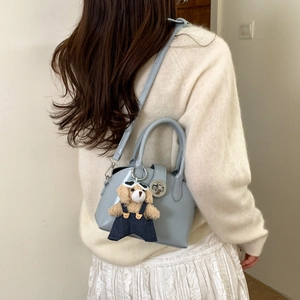 Close-up of light blue patent leather handbag with adjustable strap and cute bear charm