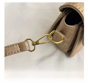 Close-up of golden metal hooks and D-ring on beige textured leather crossbody bag