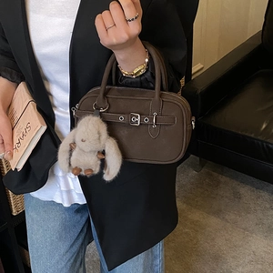 Detail of dark brown matte leather handbag featuring a silver buckle and plush rabbit charm