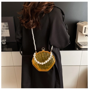 Chic amber acrylic shell bag with pearl chain shown on model in a minimalist setting