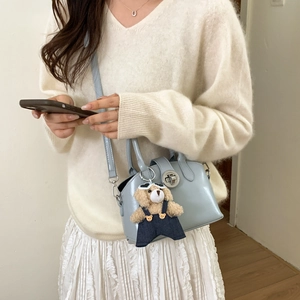 Close-up of a light blue leather handbag with silver clasp and cute bear plush charm