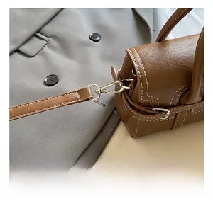 Detail showing silver metal clasp and contrast stitching on dark brown leather handbag