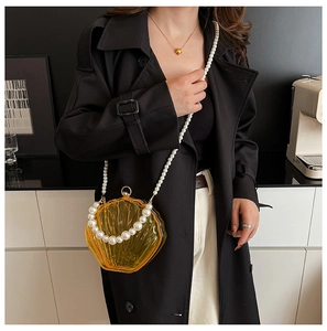 Detail view of yellow acrylic shell bag with pearl chain handle and strap for evening party