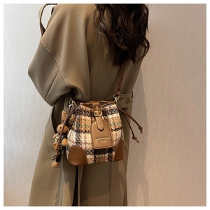 Détail du sac seau à carreaux en tweed avec bordure en cuir et breloque ours en peluche