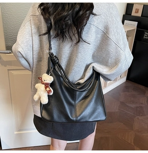 Detail of black matte leather dumpling bag with cute plush bear pendant on shoulder strap