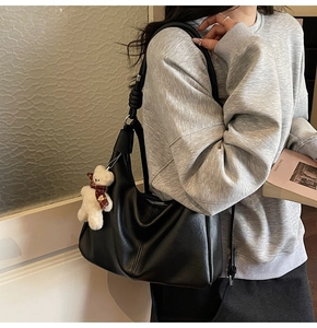 Detail view of black PU leather shoulder bag with white bear pendant and stitching