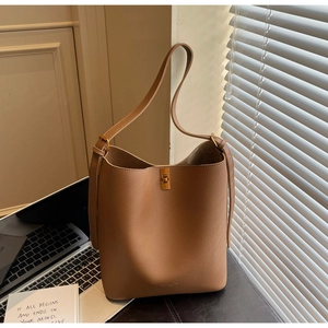 Detail of tan lychee-grain leather bucket bag with golden turn-lock and adjustable strap