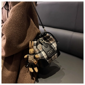 Détail du sac seau en tweed avec garniture en cuir et breloque lapin sur un siège en cuir gris
