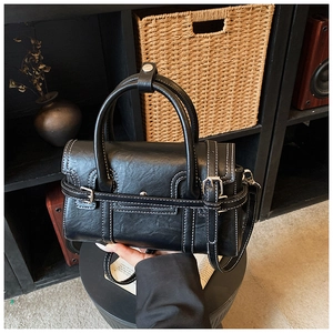 Close-up of black leather handbag with white contrast stitching and decorative metal buckle