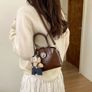 Detail of vintage brown leather bag with silver round lock and cute teddy bear charm