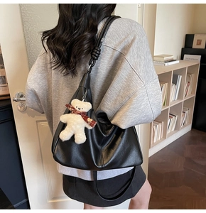 Detail of black hobo bag in matte leather featuring a cute white teddy bear charm