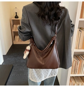 Detail of dark brown leather tote bag featuring a decorative knot and plush bear charm