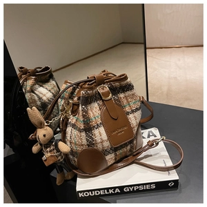 Gros plan du sac seau vintage à carreaux avec garniture en cuir et breloque lapin