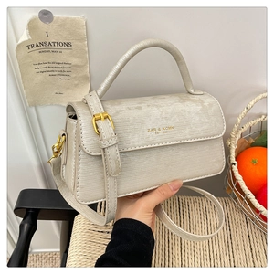 Detailed view of cream crossbody bag featuring metal buckle and textured stripe finish