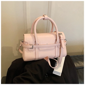 Close-up of pink PU leather handbag featuring round handles and decorative buckle strap detail