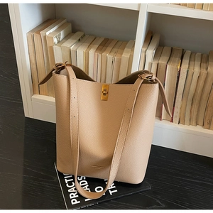 Detail of beige lychee leather bucket bag with gold clasp on books in a library