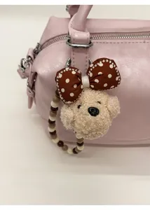 Close-up of a beige curly plush puppy charm with polka dot bow and beaded strap on a bag