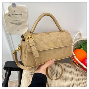 Close-up of khaki crossbody bag with fine texture and top handle on a woven chair