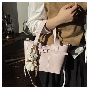 Detail shot of light pink bucket bag with leather buckle and white plush bear charm