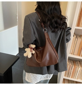 Detail view of brown hobo bag featuring a decorative knot and white teddy bear charm