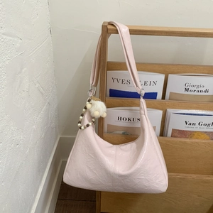 Détail d'un sac hobo rose clair plissé avec charm en peluche sur une étagère en bois