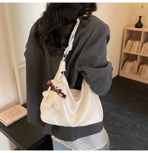 Detail of white half-moon shoulder bag featuring a knotted strap and cute plush bear charm