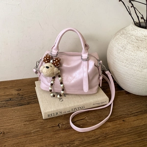 Pink faux leather Boston bag with plush bear charm on decorative book in a retro setting