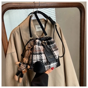 Détail du sac seau en tweed avec breloque lapin en tricot sur un trench-coat beige
