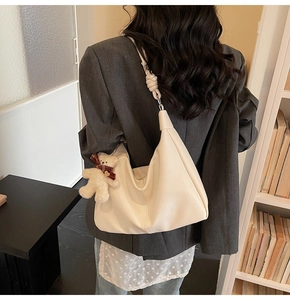 Close-up of a white leather hobo bag with a knotted strap and a cute bear charm detail