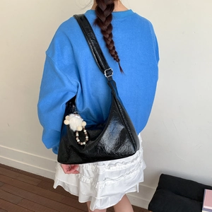 Détail du sac hobo noir brillant avec large bandoulière, boucle argentée et pompon blanc