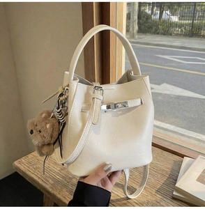Detail of cream bucket bag with lychee texture, silver lock, and bear charm accessory