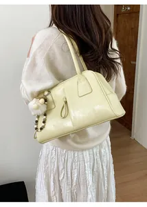 Detail of light yellow underarm bag featuring decorative drawstring and plush charm pendant