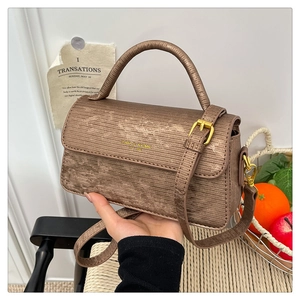 Detail of vintage brown textured crossbody bag featuring gold hardware and logo in home setting