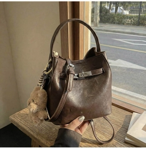 Detailed view of dark brown bucket bag with buckle strap and plush bear charm decoration