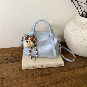 Close-up of light blue vintage boston bag with plush puppy charm on book background