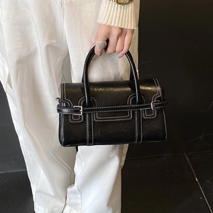 Detailed view of black leather handbag with white contrast stitching and rigid handle