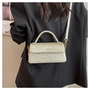 Close-up of cream square flap bag with horizontal texture and gold logo on black blazer