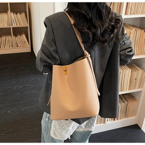 Detail of apricot pebbled leather tote bag with gold buckle on a gray blazer