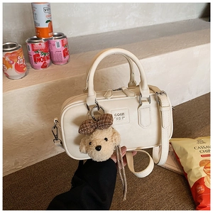 Detail of cream Boston handbag featuring embossed logo and a cute plush bear charm