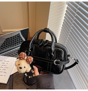 Détail d'un sac polochon noir en cuir grainé avec boucle argentée et breloque peluche