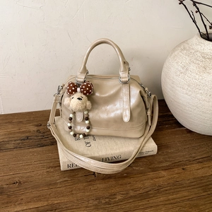 Detail of apricot glossy faux leather Boston bag with plush puppy charm on books