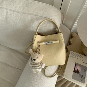 Close-up of beige lychee grain leather bucket bag with silver lock and plush bear charm