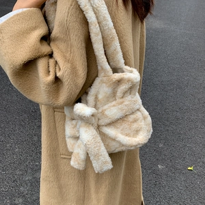 Dettaglio della borsa in peluche beige con grande fiocco indossata su cappotto cammello