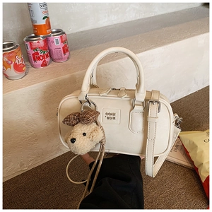 Close-up of beige PU leather Boston bag with embossed logo and cute plush bear charm